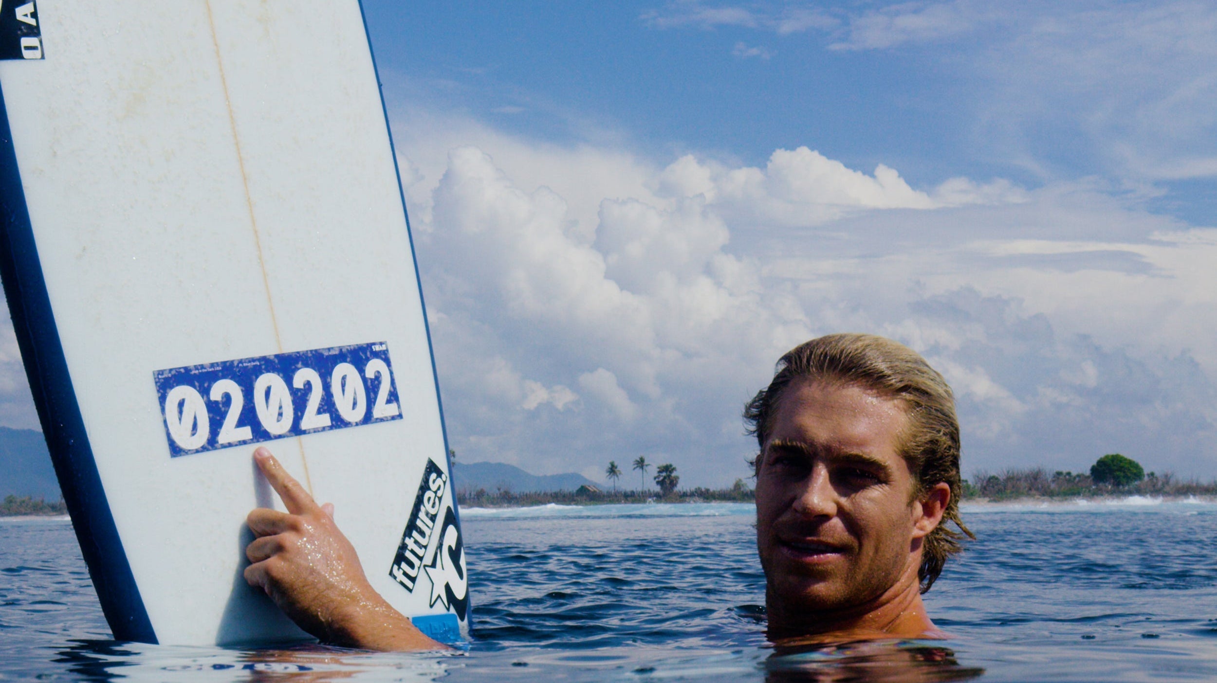 Ethan Ewing sitting in the water at Sumbawa with his finger on the 020202 number sticker of the blinded Stab in the Dark surfboard