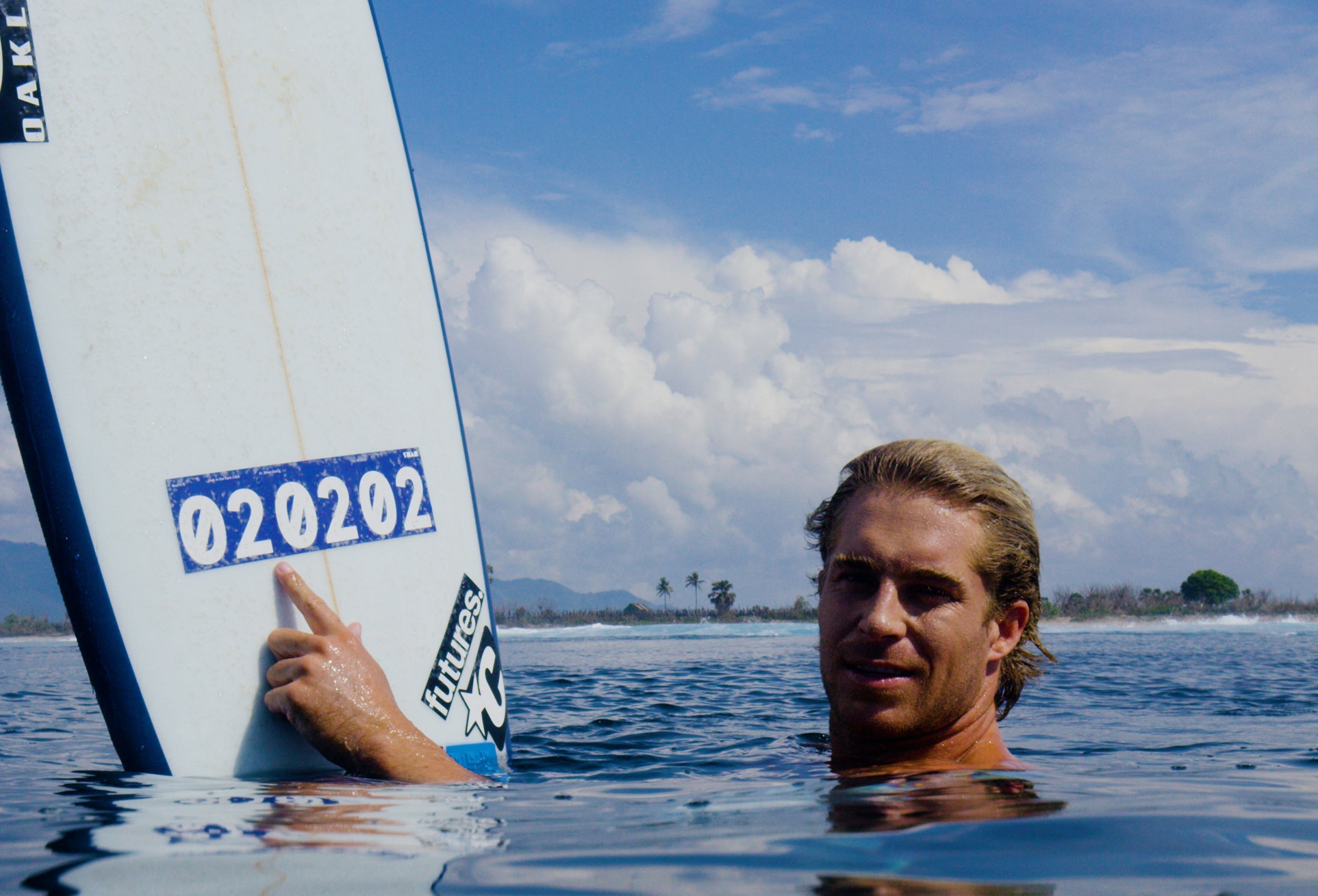 Ethan Ewing sitting in the water at Sumbawa with his finger on the 020202 number sticker of the blinded Stab in the Dark surfboard